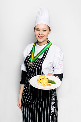 student in chefs clothing with a medal holding plate of food